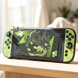Puede incluir: Una consola Nintendo Switch negra y verde con un diseño personalizado. El diseño presenta un gráfico verde y negro de una criatura. Los mandos son verdes con botones negros. La consola está sobre una superficie de madera.