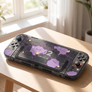 Op de afbeelding: Een zwarte Nintendo Switch console met een beschermhoes in een paars en zwart sterrenpatroon. De hoes is versierd met meerdere paarse vlekachtige figuren, kleine gele sterren en maansikkels. De console is voorzien van zwarte knoppen.