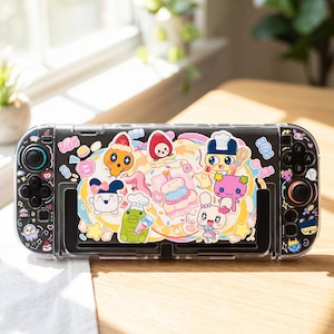 Puede incluir: Consola Nintendo Switch negra con una funda protectora transparente. La funda está decorada con personajes de dibujos animados coloridos y gráficos temáticos de comida. La consola tiene joysticks y botones negros.