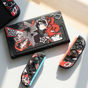 Puede incluir: Funda y Joy-Cons negros para Nintendo Switch con un diseño gráfico que presenta un personaje enmascarado, estrellas y la palabra "Wake Up". La funda y los mandos tienen detalles en rojo y blanco.