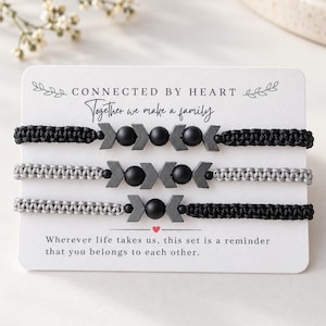 May include: Three braided cord bracelets on a white display card with the text Connected by Heart, Together we make a family, and Wherever life takes us, this set is a reminder that you belongs to each other. The bracelets feature black and grey beads.