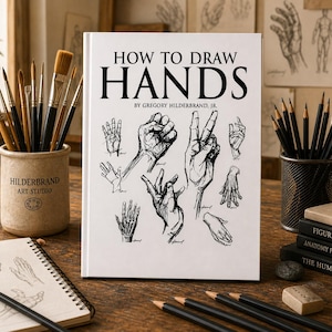 Puede incluir: Un libro titulado "HOW TO DRAW HANDS" de Gregory Hilderbrand, Jr. se muestra sobre un escritorio de madera. La portada del libro presenta bocetos de manos. Suministros de arte, incluyendo lápices, pinceles y cuadernos de bocetos, rodean el libro.