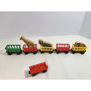 May include: A wooden toy train set consisting of one green, two red, and two yellow open-top cargo cars. Three cars carry wooden animal figures: a giraffe, an elephant with a ball, and a lion. One additional red cargo car sits in the foreground.