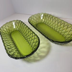 Puede incluir: Dos fuentes de vidrio verde. Cada fuente es rectangular con un patrón tejido en los lados y una base verde sólida. Las fuentes están vacías y se encuentran sobre una superficie blanca.