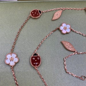 May include: Rose gold chain necklaces with ladybug, flower, and leaf charms. The ladybug charms are red with black accents, and the flower charms are white with a mother-of-pearl center. The leaf charms are textured.