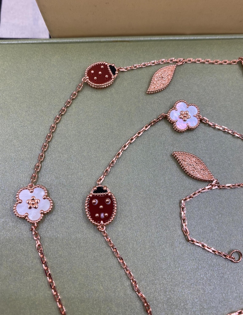 May include: Rose gold chain necklaces with ladybug, flower, and leaf charms. The ladybug charms are red with black accents, and the flower charms are white with a mother-of-pearl center. The leaf charms are textured.