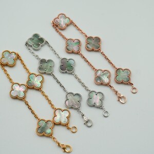 K&ouml;nnte beinhalten: Vier Armb&auml;nder mit Kleeblatt-Anh&auml;ngern. Die Armb&auml;nder sind in Gold-, Silber- und Ros&eacute;goldt&ouml;nen gehalten. Jeder Kleeblatt-Anh&auml;nger hat einen Perlmutt-Mittelteil. Die Armb&auml;nder werden auf einer wei&szlig;en Oberfl&auml;che pr&auml;sentiert.