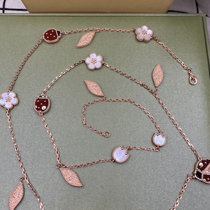 May include: Rose gold necklace with ladybug, flower, and leaf charms. The necklace features a delicate chain with alternating ladybug and flower pendants, along with leaf-shaped accents. The ladybugs have red and black details, while the flowers have white centers.