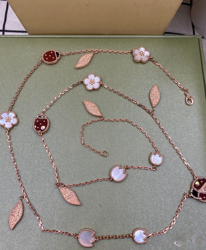 May include: Rose gold necklace with ladybug, flower, and leaf charms. The necklace features a delicate chain with alternating ladybug and flower pendants, along with leaf-shaped accents. The ladybugs have red and black details, while the flowers have white centers.