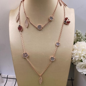 May include: Two rose gold necklaces displayed on a mannequin. One necklace features ladybug, leaf, and flower charms. The other necklace has round and leaf-shaped charms. The necklaces are delicate and elegant.