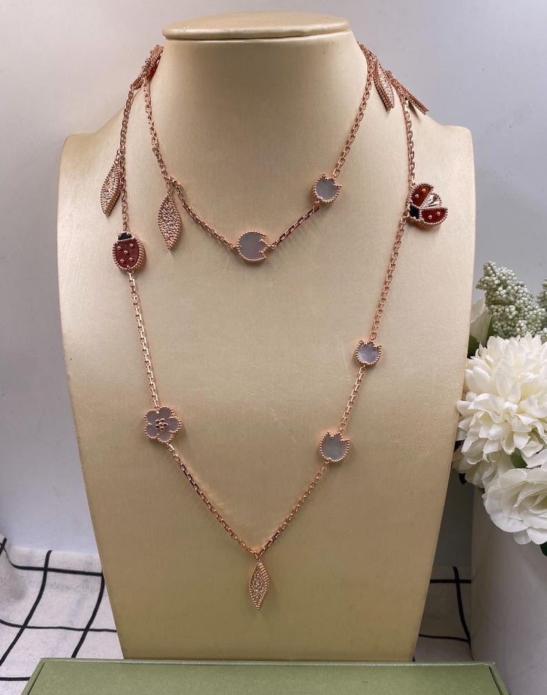 May include: Two rose gold necklaces displayed on a mannequin. One necklace features ladybug, leaf, and flower charms. The other necklace has round and leaf-shaped charms. The necklaces are delicate and elegant.