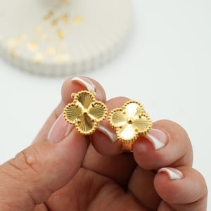 K&ouml;nnte beinhalten: Ein Paar goldfarbene Kleeblatt-Ohrringe. Jeder Ohrring hat vier Bl&uuml;tenbl&auml;tter mit einem strukturierten, geriffelten Design. Die Ohrringe werden vor einem wei&szlig;en Hintergrund gehalten.