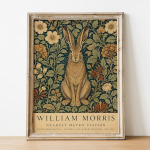 May include: A framed vertical print featuring a brown hare centered against a dark green background with intricate floral patterns in cream, orange, and rust. The text at the bottom reads WILLIAM MORRIS, NEAREST METRO STATION, SOUTH KENSINGTON, VICTORIA AND ALBERT MUSEUM, SW7 2RL.