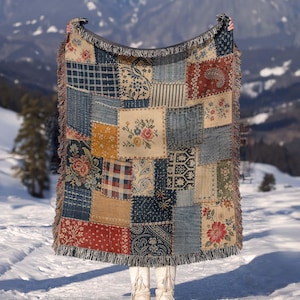 May include: A woven throw blanket featuring a patchwork design of various fabric patterns including floral motifs, plaid, stripes, and paisley in shades of blue, red, yellow, and cream. The blanket has a fringed edge and a textured, multi-panel appearance.