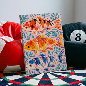 May include: A rectangular canvas print featuring three koi fish stacked vertically against a light pink background with teal seaweed patterns. The top fish is orange, white, and black; the middle fish is orange and yellow; the bottom fish is blue and white.