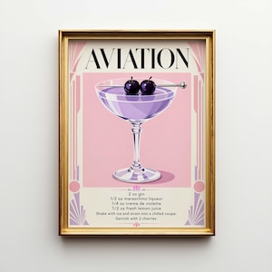 May include: A framed art print featuring a cocktail recipe for an Aviation. The print has a gold frame and a pink and purple color scheme. The word "AVIATION" is at the top. The recipe includes gin, maraschino liqueur, creme de violette, and lemon juice, garnished with cherries.