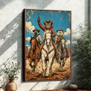 May include: A framed art print depicts three cats riding horses in a Western scene. The lead cat, wearing a cowboy hat and red bandana, holds a gun. The artwork has a vintage, distressed look with a blue sky and desert landscape.
