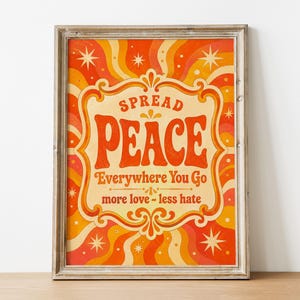 May include: A framed wall art print featuring a wavy orange, red, and yellow background with star accents. The text reads SPREAD PEACE Everywhere You Go and more love - less hate, centered within a decorative border in a bold, retro-style font.
