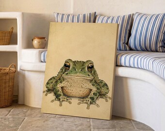 May include: A rectangular canvas print featuring a detailed illustration of a green toad with dark spots and large, expressive eyes. The toad is centered on a solid, light beige background, showcasing its textured skin and webbed feet.