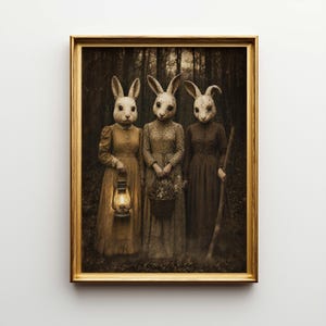 May include: A framed sepia-toned print featuring three figures with rabbit heads in vintage dresses standing in a forest. One holds a lantern, another a basket, and the third a staff. The artwork has a surreal, slightly eerie quality.