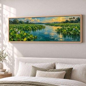 May include: A panoramic landscape painting in a wooden frame depicting a calm river winding through lush green lily pads and aquatic vegetation under a golden sunset sky with soft clouds and distant trees along the horizon line.