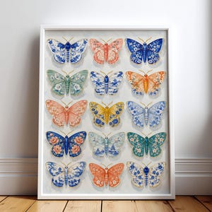 Op de afbeelding: Een ingelijste rechthoekige wandkunstprint met een raster van vijftien vlinders. Elke vlinder toont een uniek patroon, waaronder blauw-witte porseleinstijl motieven, evenals oranje, gele, groene en bloemrijke ontwerpen op een lichte achtergrond.