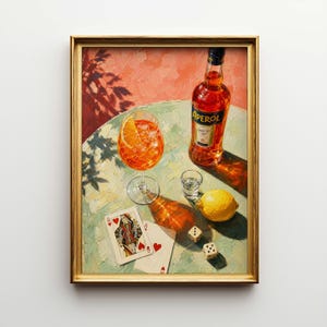 May include: A framed painting depicts a cocktail scene with an Aperol bottle, a glass of orange cocktail, a shot glass, a lemon, playing cards, and dice on a table. The painting has a gold frame and a light green and pink background.