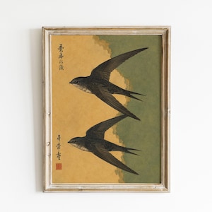 Könnte beinhalten: Ein gerahmter Kunstdruck mit zwei dunkelbraunen Schwalben im Flug vor einem geteilten Hintergrund in Senfgelb und gedämpftem Olivgrün. Das Kunstwerk enthält vertikale schwarze japanische Kalligrafie auf der linken Seite und ein kleines rotes Quadrat.