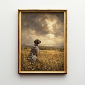 Op de afbeelding: Een ingelijst schilderij toont een Duitse Staande Hond in een veld met gele wilde bloemen. De hond heeft bruin en wit gevlekt haar. De achtergrond toont een landschap onder een bewolkte hemel met een gouden gloed.