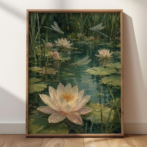 Op de afbeelding: Een ingelijste kunstdruk met een vijvertafereel met lichtroze waterlelies, groene leliebladeren en hoog riet. Drie libellen met doorschijnende vleugels zweven boven het water, dat het omringende groen in donkere tinten weerspiegelt.