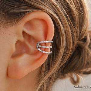 Puede incluir: Un ear cuff plateado con tres filas de cristales claros y brillantes. El ear cuff se lleva en la parte superior de la oreja, añadiendo un toque de elegancia. Un accesorio moderno.
