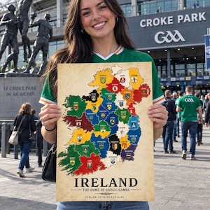 May include: A rectangular poster featuring a map of Ireland divided into coloured counties, each marked with a crest. The text reads IRELAND THE HOME OF GAELIC GAMES and CUMANN LUTHCHLEAS GAEL. The background has a vintage, aged paper appearance.
