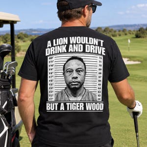 May include: A black short-sleeved t-shirt featuring a white graphic print of a mugshot with height markers. The text reads A LION WOULDN'T DRINK AND DRIVE BUT A TIGER WOOD. The design includes a portrait of a person centred between the measurement lines.