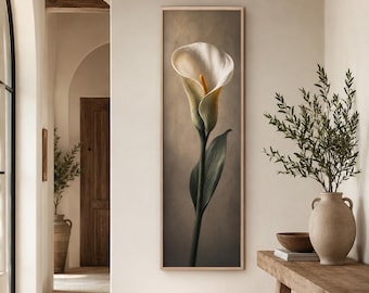 May include: A vertical rectangular wall art piece featuring a single white calla lily flower with a prominent yellow spadix and a long green stem. The artwork is encased in a light-colored wooden frame and displayed against a neutral wall.