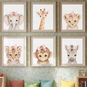 May include: Six framed animal prints with watercolor illustrations of an elephant, giraffe, lion cub, tiger cub, monkey, and zebra, each wearing a pink bow. The prints are displayed on a wall in a child's room, above a bench with colorful pillows.