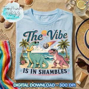 May include: Light blue t-shirt with a beach scene featuring two dinosaurs wearing sunglasses. The text "The Vibe Is In Shambles" is displayed above the dinosaurs. The design includes palm trees, a sunset, and a meteor.