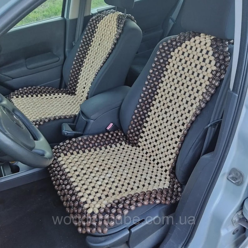 May include: Two car seat covers made of small, smooth wooden beads arranged in a grid pattern. The design features a central panel of light beige beads bordered by dark brown beads, covering the backrest and seat area of the vehicle seats.
