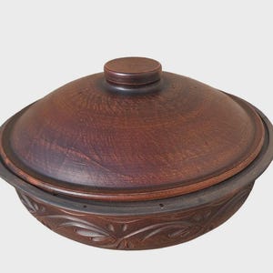 Könnte beinhalten: Eine braune Keramik-Auflaufform mit Deckel. Die Form hat eine runde Form mit einem dekorativen floralen Muster um den Boden. Der Deckel hat einen kleinen, runden Griff. Die Form ist zum Kochen und Servieren bestimmt.