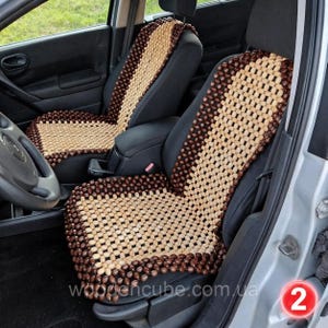 May include: A pair of car seat covers constructed from small, polished wooden beads. The covers feature a central panel of light tan beads surrounded by a border of dark brown beads, designed to fit over the front seats of a vehicle interior.