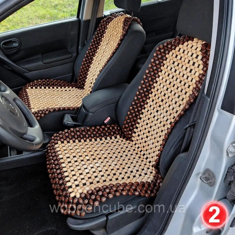 May include: A pair of car seat covers constructed from small, polished wooden beads. The covers feature a central panel of light tan beads surrounded by a border of dark brown beads, designed to fit over the front seats of a vehicle interior.
