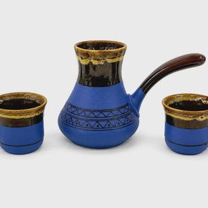 Peut inclure: Un ensemble à café en céramique composé d'une cafetière centrale à long manche et de deux tasses assorties. Chaque pièce présente une base bleu vif, une section supérieure brun foncé et un bord brun texturé avec un motif géométrique.