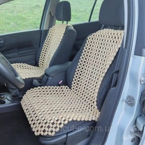 May include: Two car seat covers made of light beige wooden beads arranged in a grid pattern. The covers are placed over the front driver and passenger seats of a vehicle, featuring a flexible design that conforms to the seat shape.