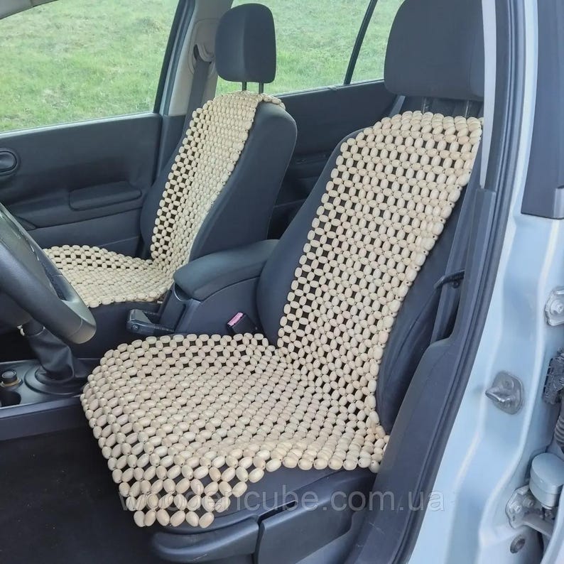 May include: Two car seat covers made of light beige wooden beads arranged in a grid pattern. The covers are placed over the front driver and passenger seats of a vehicle, featuring a flexible design that conforms to the seat shape.