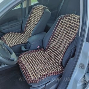 May include: A set of two car seat covers made from small, rounded wooden beads in alternating light beige and dark brown colors. The beads are arranged in a grid pattern and are designed to cover the backrest and seat cushion of vehicle seats.
