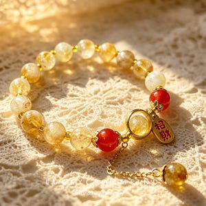 Pode incluir: Uma pulseira de contas com contas de citrino amarelo translúcido e duas contas vermelhas lisas. Inclui um anel de metal dourado, um pequeno pingente dourado com os caracteres chineses vermelhos 招財 e uma corrente pendente com uma conta.