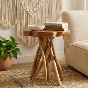 May include: A round side table constructed from natural light brown wood with a thick, uneven edge top and a base formed by several interlocking, branch-like wooden legs. A white bowl and a stack of two books are placed on the table surface.
