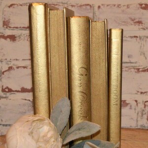 May include: A set of five gold-painted books with titles visible on the spines. The titles are "The Teacher Who Couldn't Read", "Robert Moore", "Inn Creek", and "The Fate of Doom".