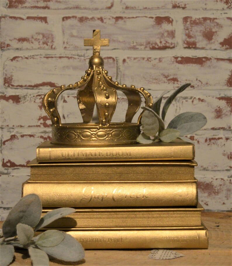 May include: A gold crown sits atop a stack of gold-painted books. The books have titles such as "Ultimate Doom" and "Gap Creek".