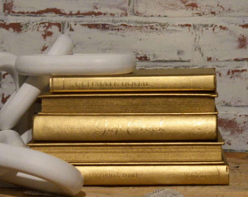 May include: A stack of five gold-coloured hardback books. The top book has the title "Ultimate Doom" on the spine. The second book has the title "Gap Creek" on the spine. The third book has the title "Robert Novak" on the spine. The fourth book has the title "A Soulful Read" on the spine. The bottom book has the title "The Ultimate Guide to" on the spine.