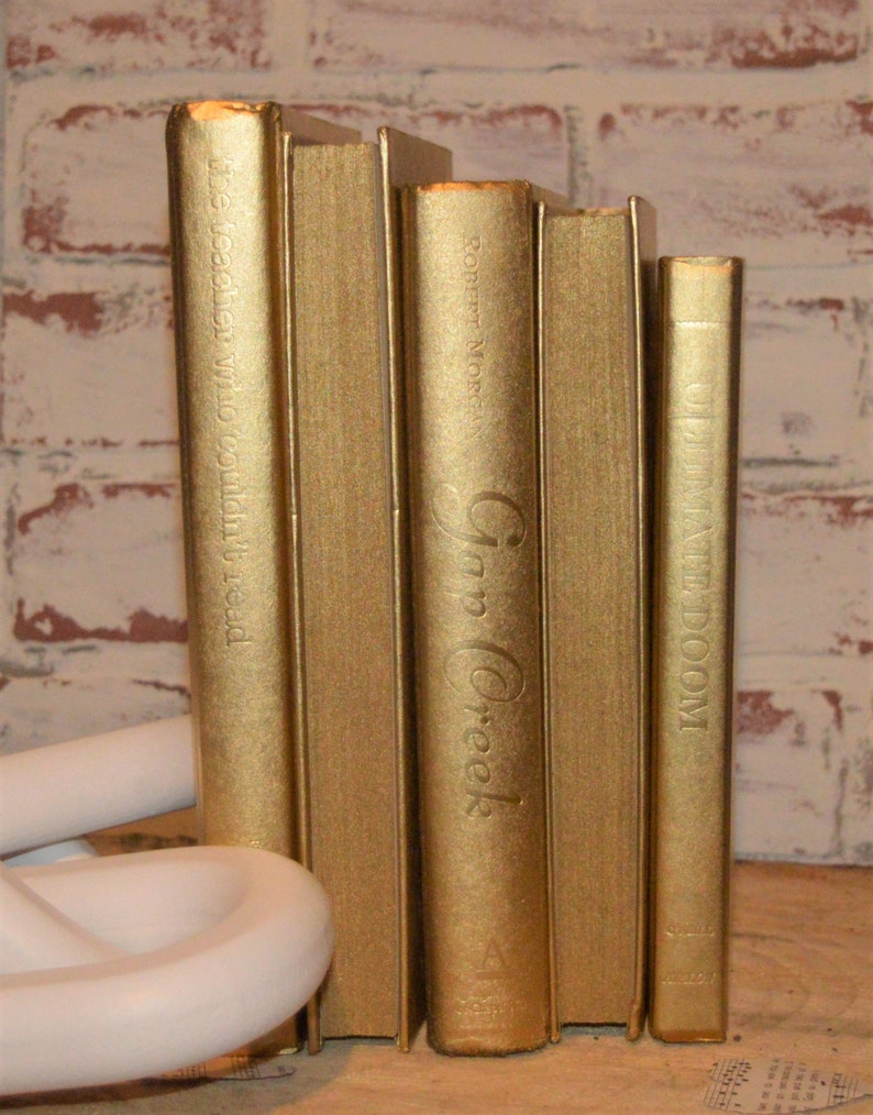 May include: Five gold-coloured hardcover books with titles visible on the spines. The titles are "The Teacher Who Couldn't Read", "Robert Morgan", "Gap Creek", "D", and "Unwind Doom".
